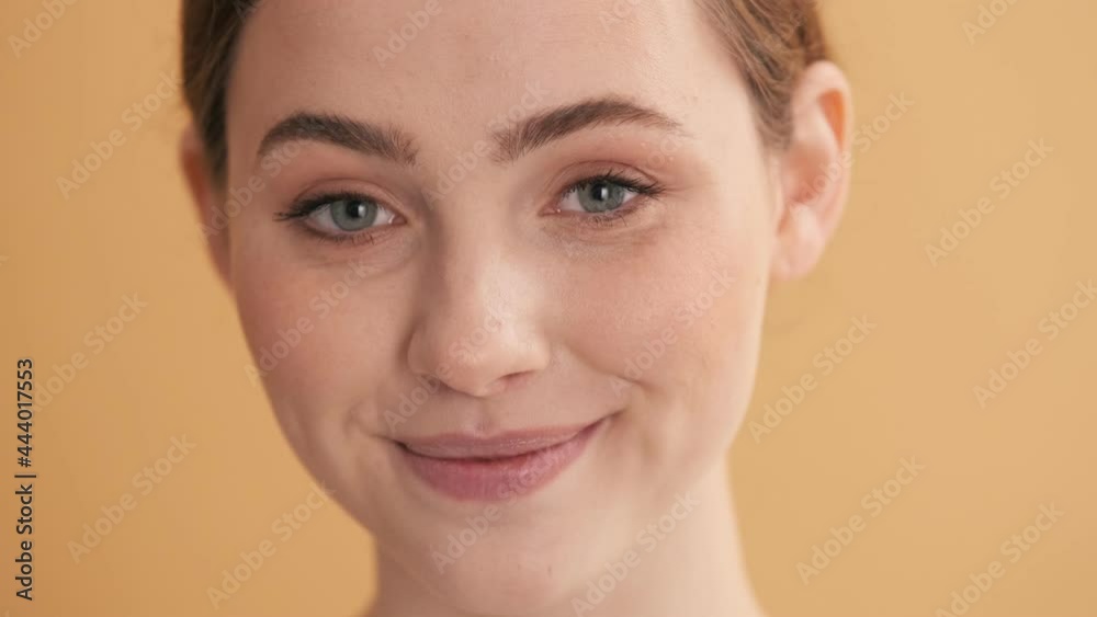 A close-up view of a happy woman is looking aside while posing to the camera standing isolated over beige wall in the studio A close-up view of a happy woman is looking aside while posing to the camera standing isolated over beige wall in the studio