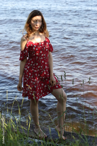 Slender woman in red dress at a sea shore with shadows and light on her