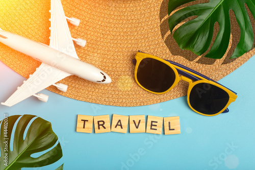 Travel summer background. Sunglasses, hat, palm tropical leaves, airplane and beach accessories on a colored blue background. Tourist vacation, relaxation and summer concept.