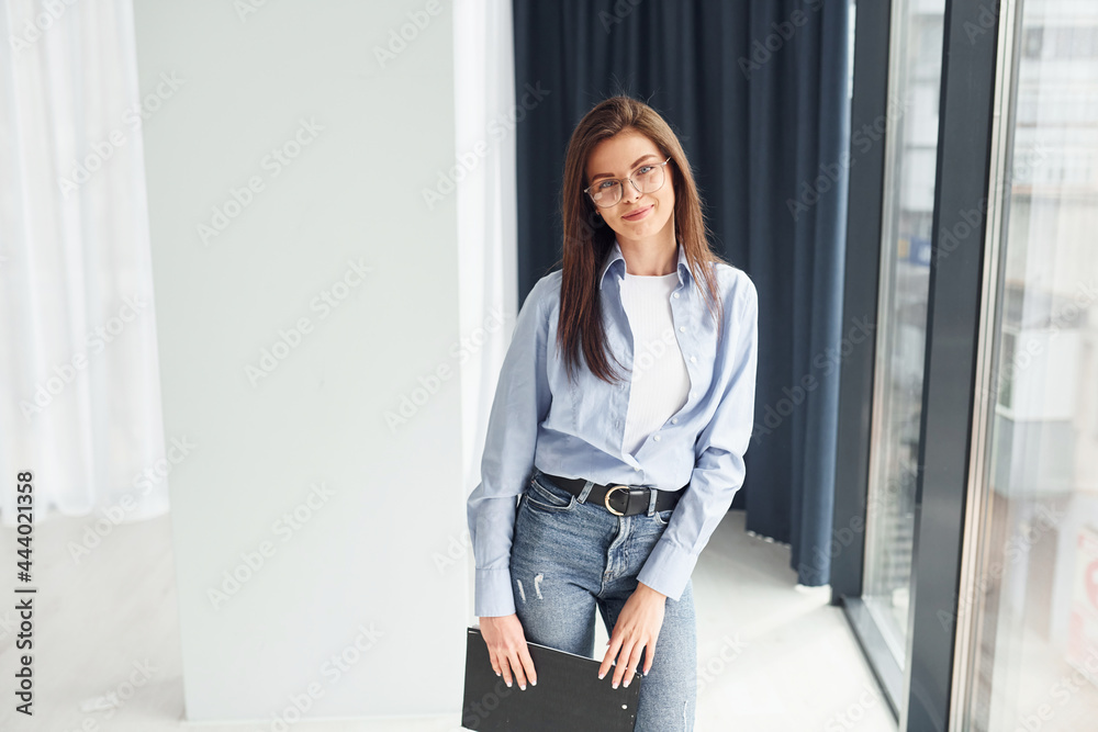 Fototapeta premium Young woman in glasses, formal clothes and with notepad standing indoors