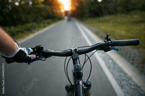 First person view of handling the bicycle on the empty asphalt road in the city towards sunlight