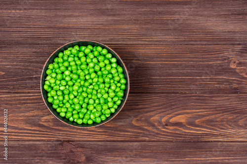 Fresh green peas in a bowl on a brown wooden table. View from above. Place for an inscription.