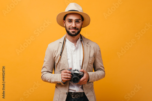 Smiling man in beige outfit holding retro camera on orange background
