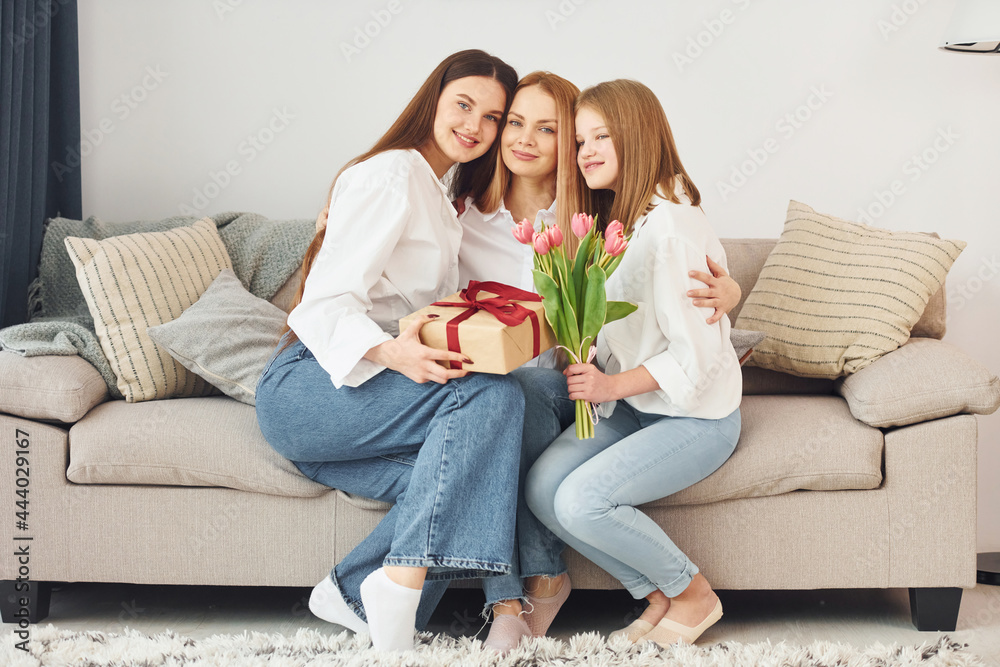 Making surprise with flowers. Young mother with her two daughters at home at daytime Making surprise with flowers. Young mother with her two daughters at home at daytime