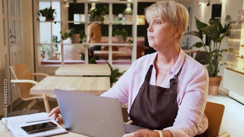 A serious woman cafe worker is working with receipt while using her mobile sitting at table in cafe A serious woman cafe worker is working with receipt while using her mobile sitting at table in cafe