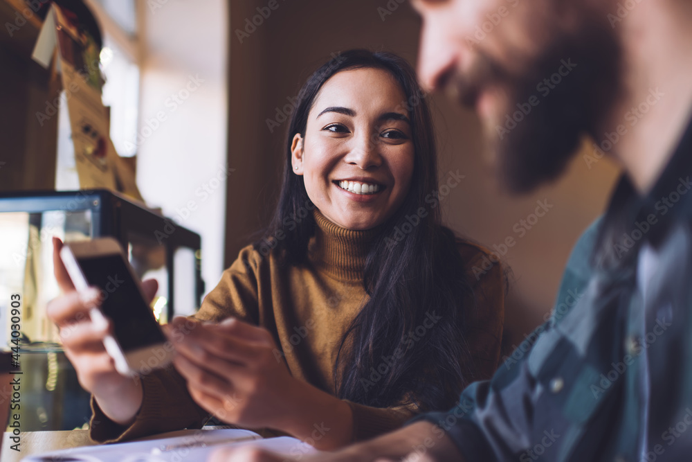 Smiling young lady showing smartphone to boyfriend while sitting in cafe Smiling young lady showing smartphone to boyfriend while sitting in cafe