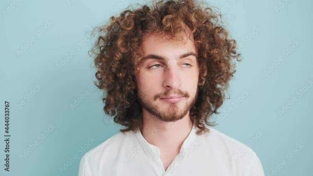 A curly man is ponding while looking to the camera standing isolated over blue background A curly man is ponding while looking to the camera standing isolated over blue background