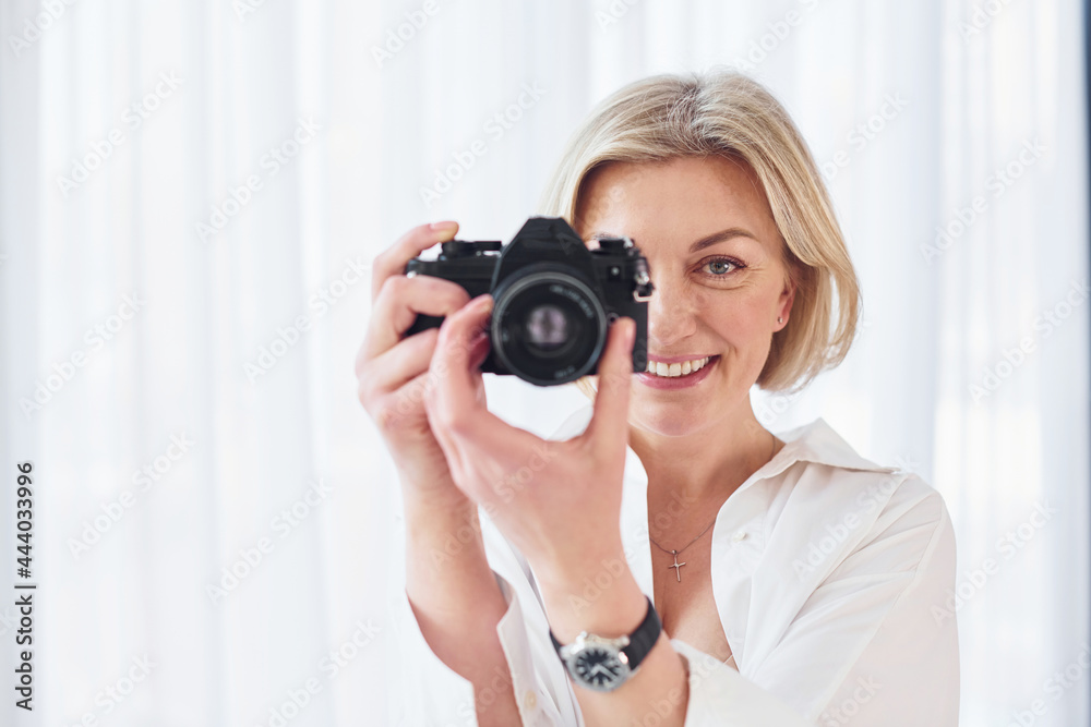 Middle-aged woman in elegant clothes is at home. Photographer with camera