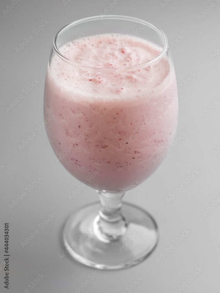 Delicious cold raspberry milkshake in glass on gray background