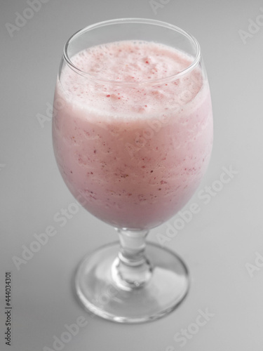 Delicious cold raspberry milkshake in glass on gray background