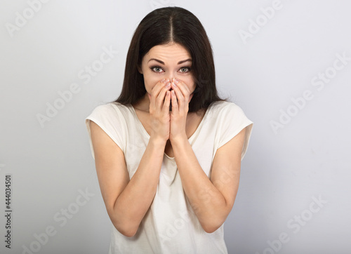 Beautiful young casual cute chuckle woman  covering the face the hands on blue background. Closeup portrait