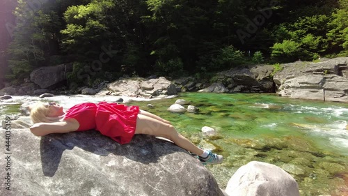 Woman relaxing sitting on the rocks of the Verzasca river. Verzasca valley by Lavertezzo town. Famous landmark for riverside leisure and high diving in Ticino, Switzerland. photo