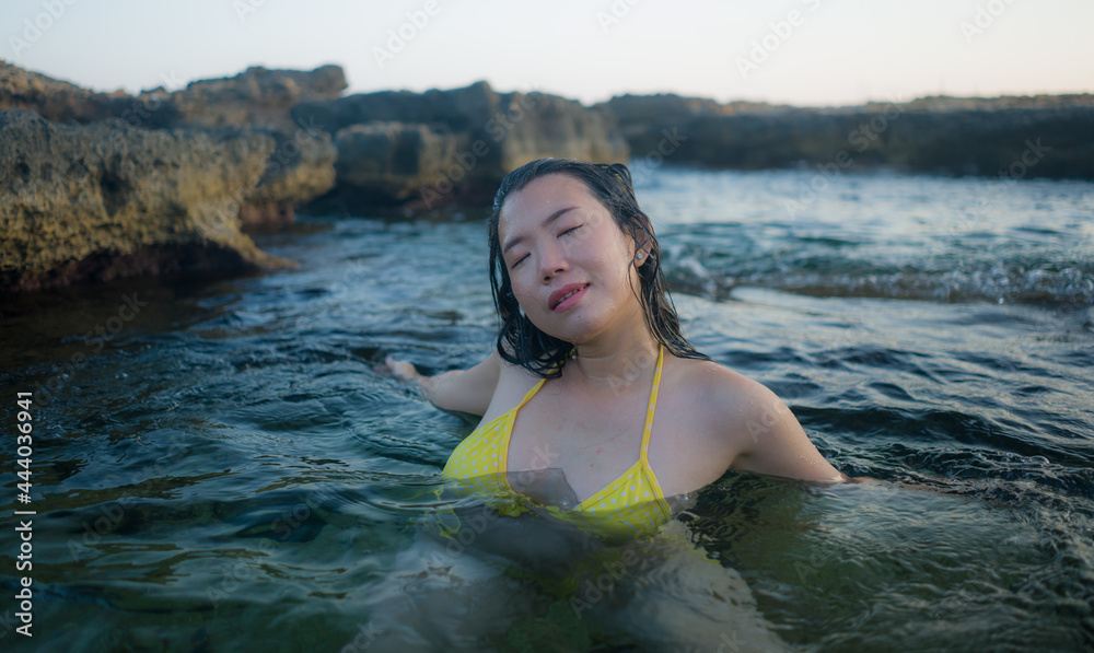Fototapeta premium summer lifestyle portrait of young attractive and happy Asian woman swimming in the sea - beautiful Korean girl in yellow bikini enjoying tropical island holidays