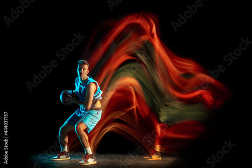 Professional male basketball player in blue uniform playing basketball isolated over dark studio background in mixed light. Concept of healthy lifestyle, professional sport, hobby. © master1305