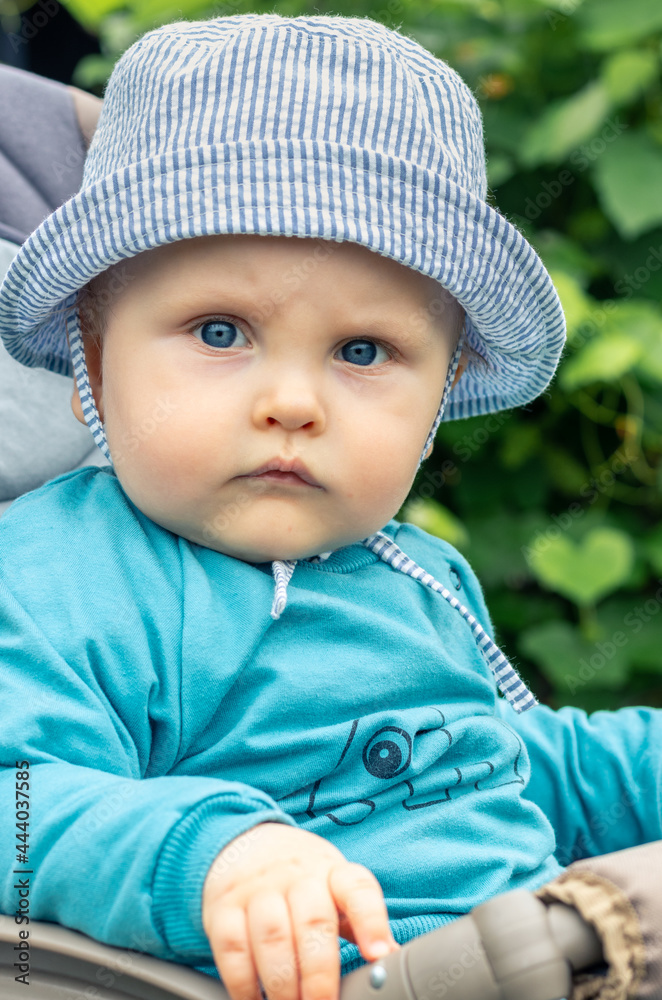 Portrait of serious unsmiling baby wearing sunhat and sitting in the baby buggy. Childhood, cute child concept. Portrait of serious unsmiling baby wearing sunhat and sitting in the baby buggy. Childhood, cute child concept.