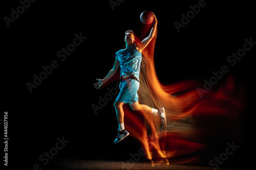 Young caucasian man, male basketball player playing basketball isolated over dark studio background in mixed light. Concept of healthy lifestyle, professional sport, hobby.