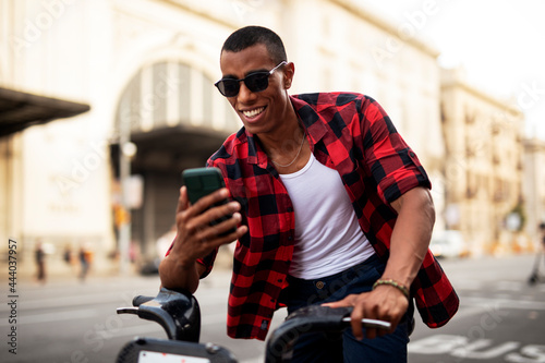 Portrait of handsome african man using electric bike in the city. Happy young man using the phone...