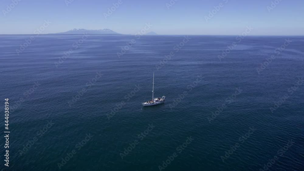 Circling shot from drone of yacht in a middle of oceanic landscape. Small boat with crew and mountains on background. Ship in still waters of Pacific ocean on bright day. Concept of travel, adventure. Circling shot from drone of yacht in a middle of oceanic landscape. Small boat with crew and mountains on background. Ship in still waters of Pacific ocean on bright day. Concept of travel, adventure.