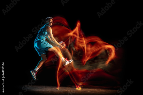 Fototapeta Naklejka Na Ścianę i Meble -  Young caucasian male basketball player playing basketball isolated over dark studio background in mixed light. Concept of healthy lifestyle, professional sport, hobby.