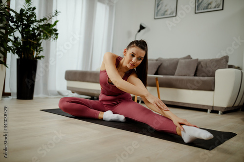 Athletic woman in sportswear doing fitness stretching exercises at home in the living room.