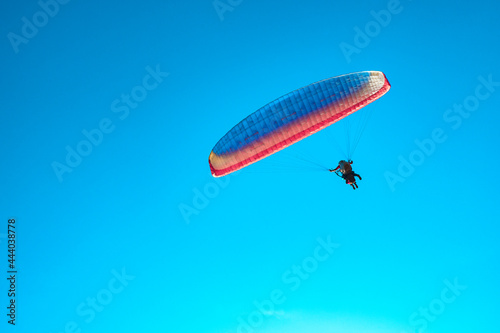 Doubles paragliding against a clear blue sky. A multi-colored papaplan flies in the clear sky closeup.
