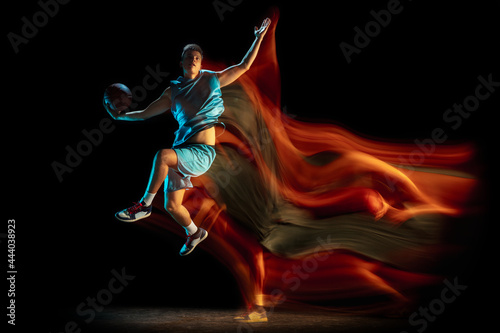 Young caucasian male basketball player playing basketball isolated over dark studio background in mixed light. Concept of healthy lifestyle, professional sport, hobby. © master1305