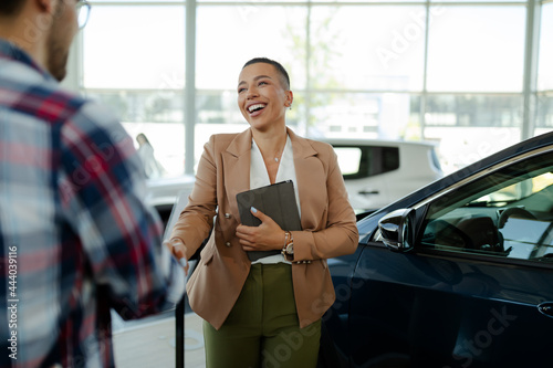 Принти на полотні Beautiful smiling saleswoman shaking hands with her male Caucasian client after selling a new car