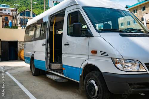 Tourist minibus is waiting with the door open in the parking lot. White minibus is parked in sunny weather.