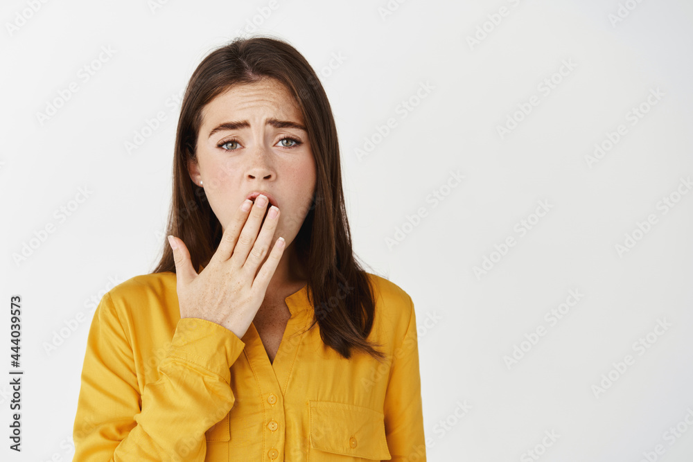 Tired young woman yawning, covering her mouth with palm and looking exhausted or bored, standing over white background Tired young woman yawning, covering her mouth with palm and looking exhausted or bored, standing over white background