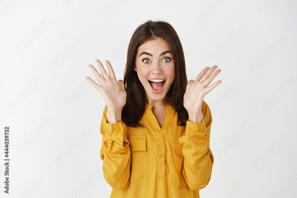 Image of surprised and excited young woman reacting to amazing news, raising hands up and scream of joy, receive a gift, standing over white background Image of surprised and excited young woman reacting to amazing news, raising hands up and scream of joy, receive a gift, standing over white background