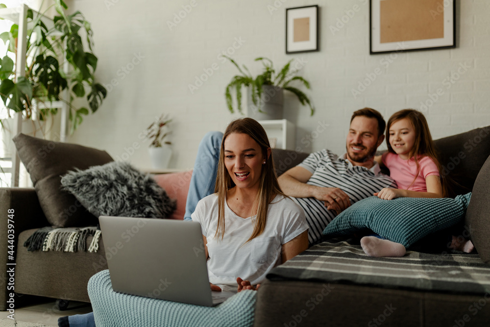 Mom freelancer is working at home, sitting on the floor while dad and daughter having fun on sofa. Mom freelancer is working at home, sitting on the floor while dad and daughter having fun on sofa.