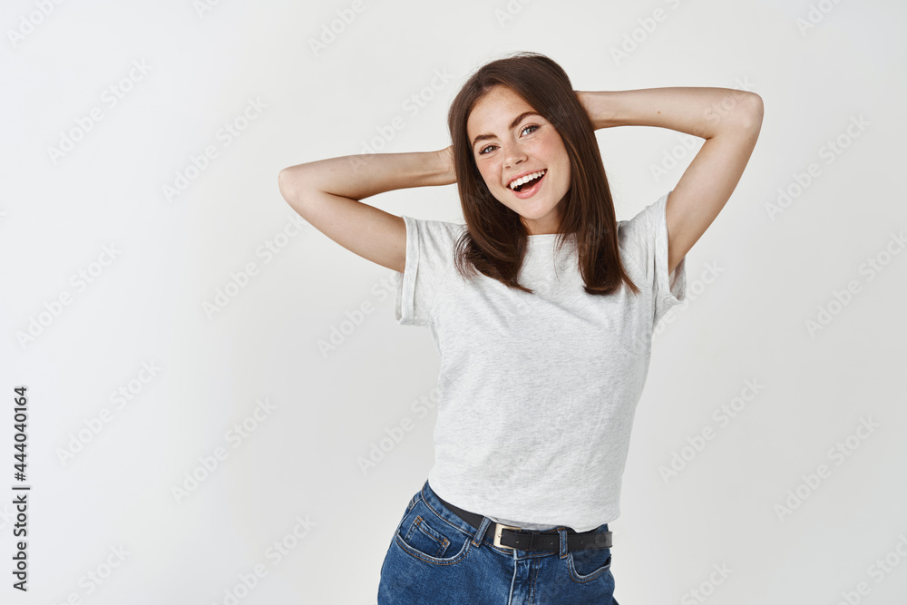 Beauty. Happy and relaxed young woman looking carefree at camera, holding hands behind head, resting against white background Beauty. Happy and relaxed young woman looking carefree at camera, holding hands behind head, resting against white background