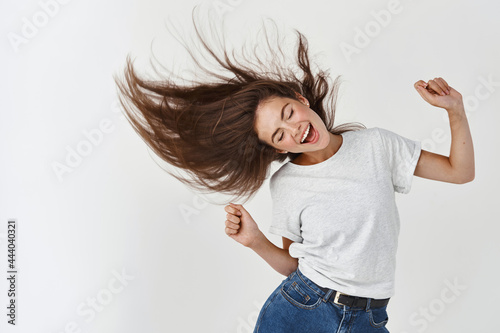 Haircare and beauty concept. Happy young woman dancing and whip healthy shiny hair, having fun, standing joyful over white background