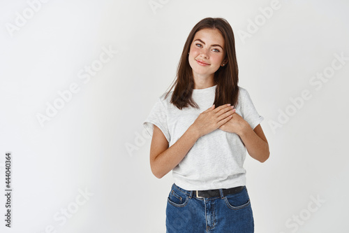 Photography Young woman in casual t-shirt holding hands on heart and smiling with care and l