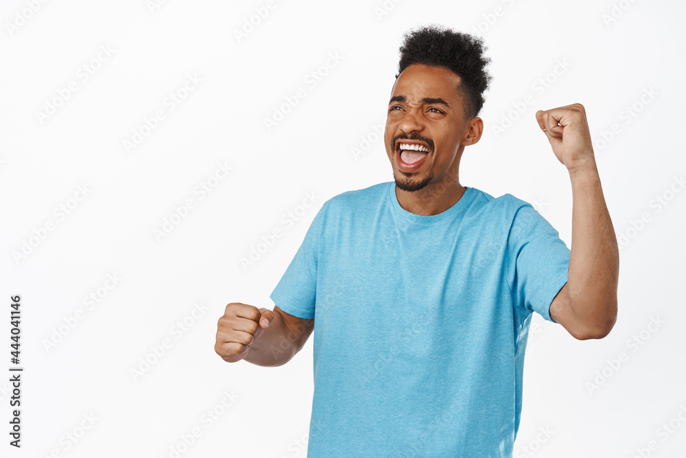 Image of cheerful african american man chanting, rooting for sport team, watching game event and shouting to support, fan fist pump and looking up, standing against white background Image of cheerful african american man chanting, rooting for sport team, watching game event and shouting to support, fan fist pump and looking up, standing against white background