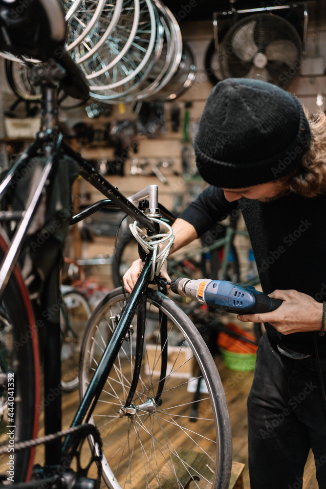 Man with screwdriver repairing bicycle in workshop Man with screwdriver repairing bicycle in workshop