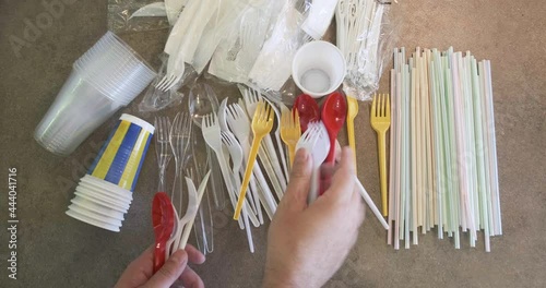 Hand adds plastic cutlery on table with single use plastic items banned in the European Union: straws, cutlery, cups, stirrers.