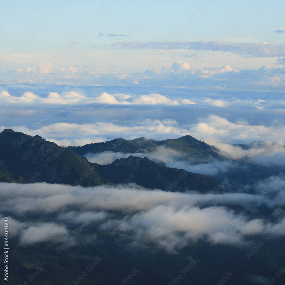 Fototapeta premium Fog and clouds surrounding green hills and mountains in Entlebuch, Lucerne Canton.