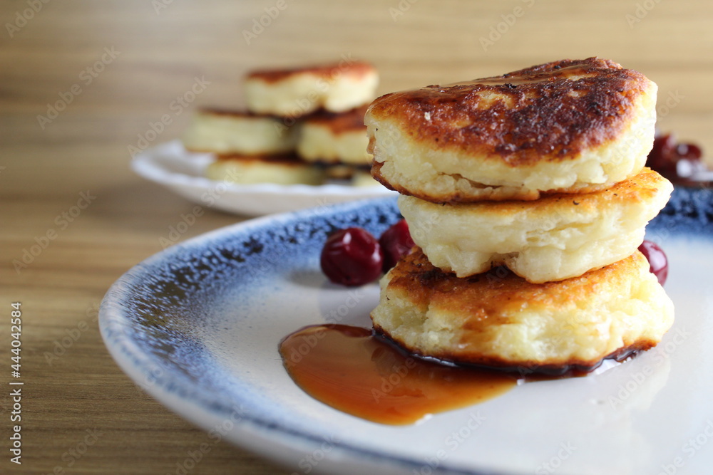Three pancake cheesecakes lie stack of slides on top of each other on plate table with cherry cherry . View from the side. Breakfast is Russian Ukrainian. Dishes cottage cheese. Place with copyspace Three pancake cheesecakes lie stack of slides on top of each other on plate table with cherry cherry . View from the side. Breakfast is Russian Ukrainian. Dishes cottage cheese. Place with copyspace