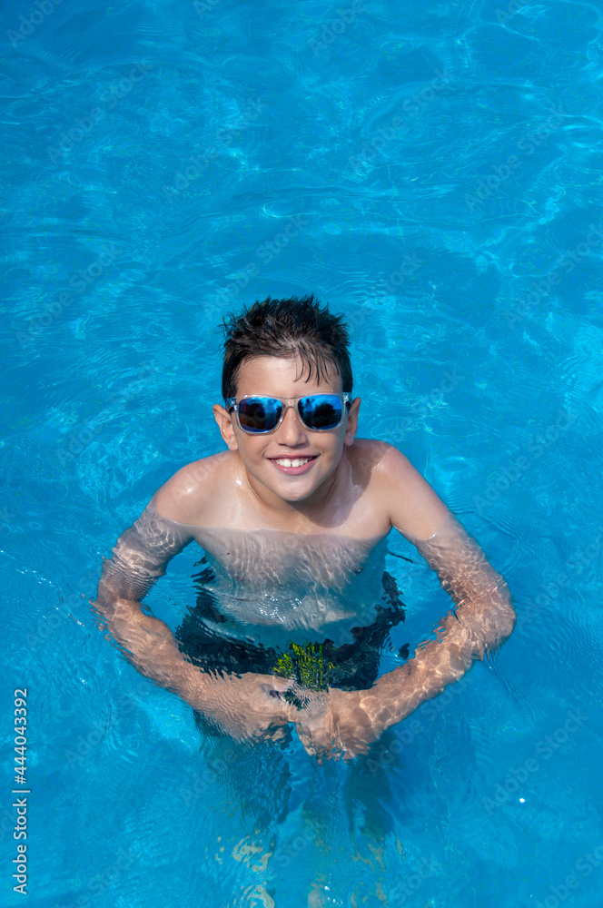 Young boy in clear blue water of swimming pool with reflecting sunglasses, resting, enjoying. Concept summer relax and chill, summer break