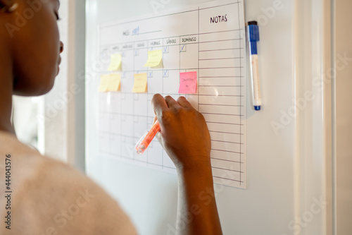 Crop black woman taking notes in planner on fridge