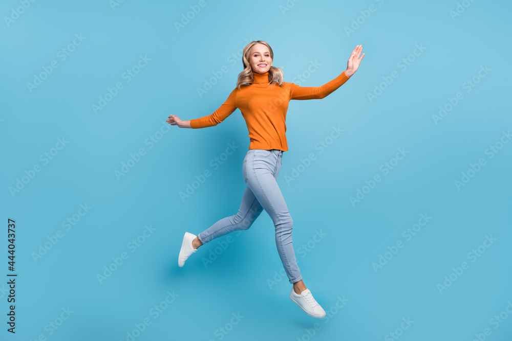 Photo of pretty adorable young lady wear orange sweater jumping high smiling isolated blue color background
