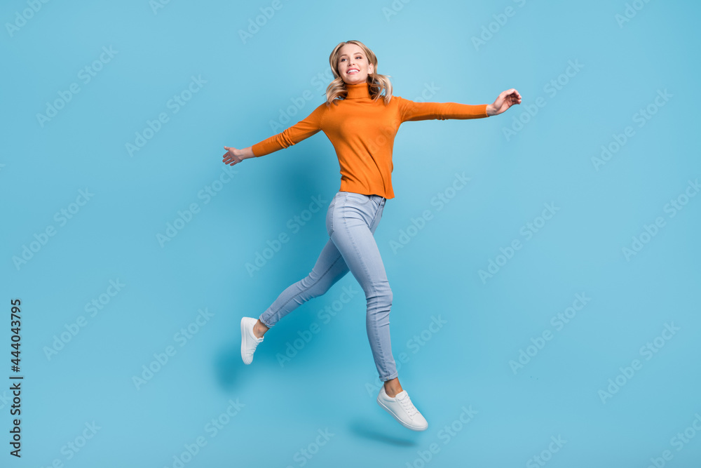 Photo of charming shiny young woman dressed orange pullover smiling jumping high isolated blue color background