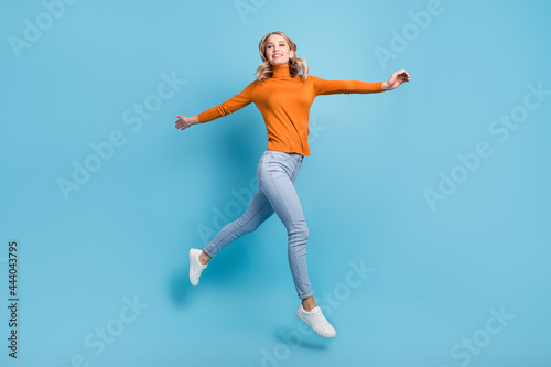 Photo of charming shiny young woman dressed orange pullover smiling jumping high isolated blue color background © deagreez