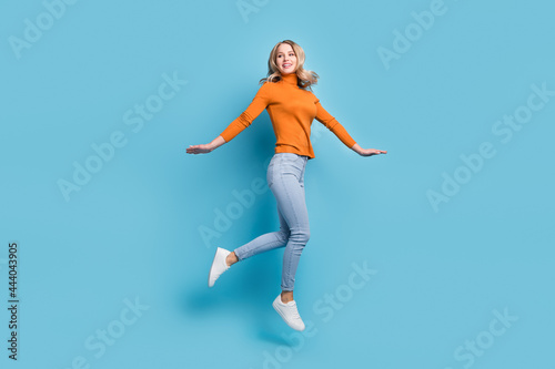 Full length photo of cheerful young woman look empty space jump up air isolated on pastel blue color background