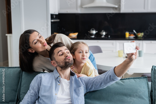 parents with daughter pouting lips while taking selfie on mobile phone at home