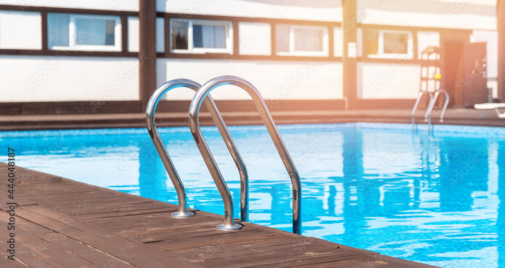 Metal ladder to enter pool, clear blue water, glint of sunlight. Concept summer party friends