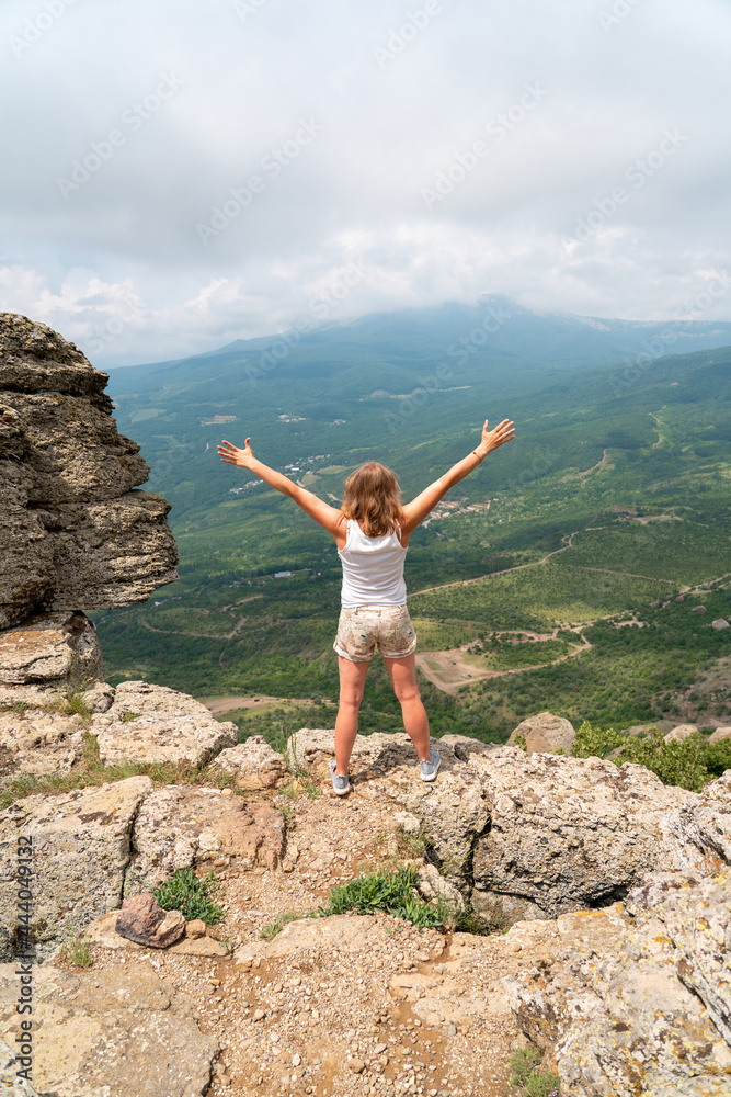 Woman raising hands up on top of mountain and looking to valley and peaks below. Healthy outdoors lifestyle concept