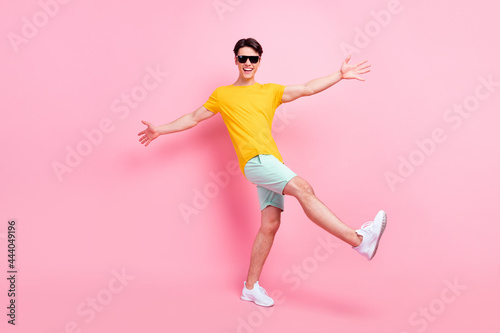 Fototapeta Naklejka Na Ścianę i Meble -  Photo of attractive funky young man wear yellow t-shirt dark eyewear smiling walking dancing isolated pink color background