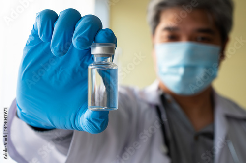 An Asian male doctor wears a medical glove and face mask holding syringe taking covid 19 coronavirus vaccine to study and analyze antibody samples for the patient. Concept of diseases, medical care